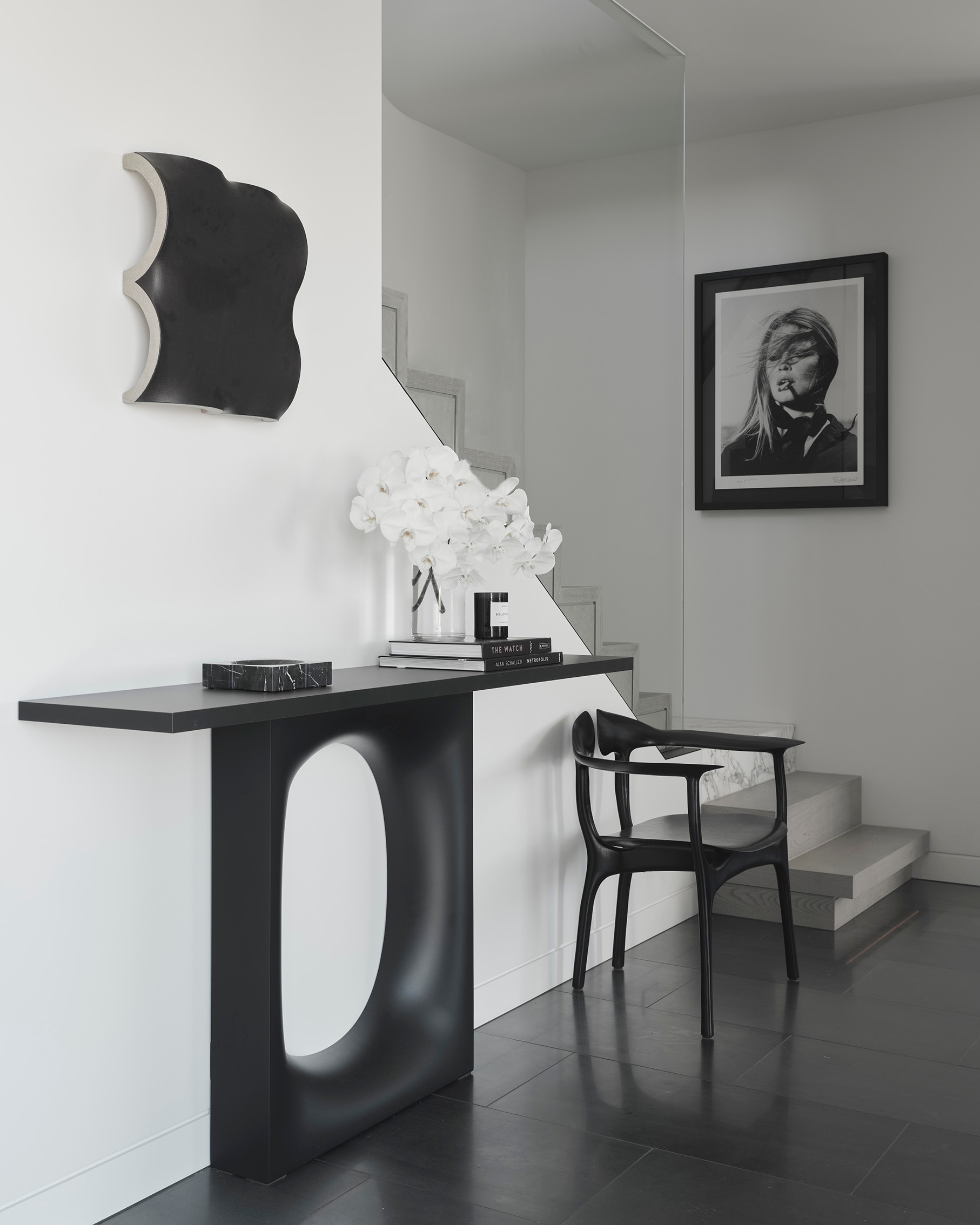 Entry vignette with a sculptural console, a framed portrait and a single white orchid