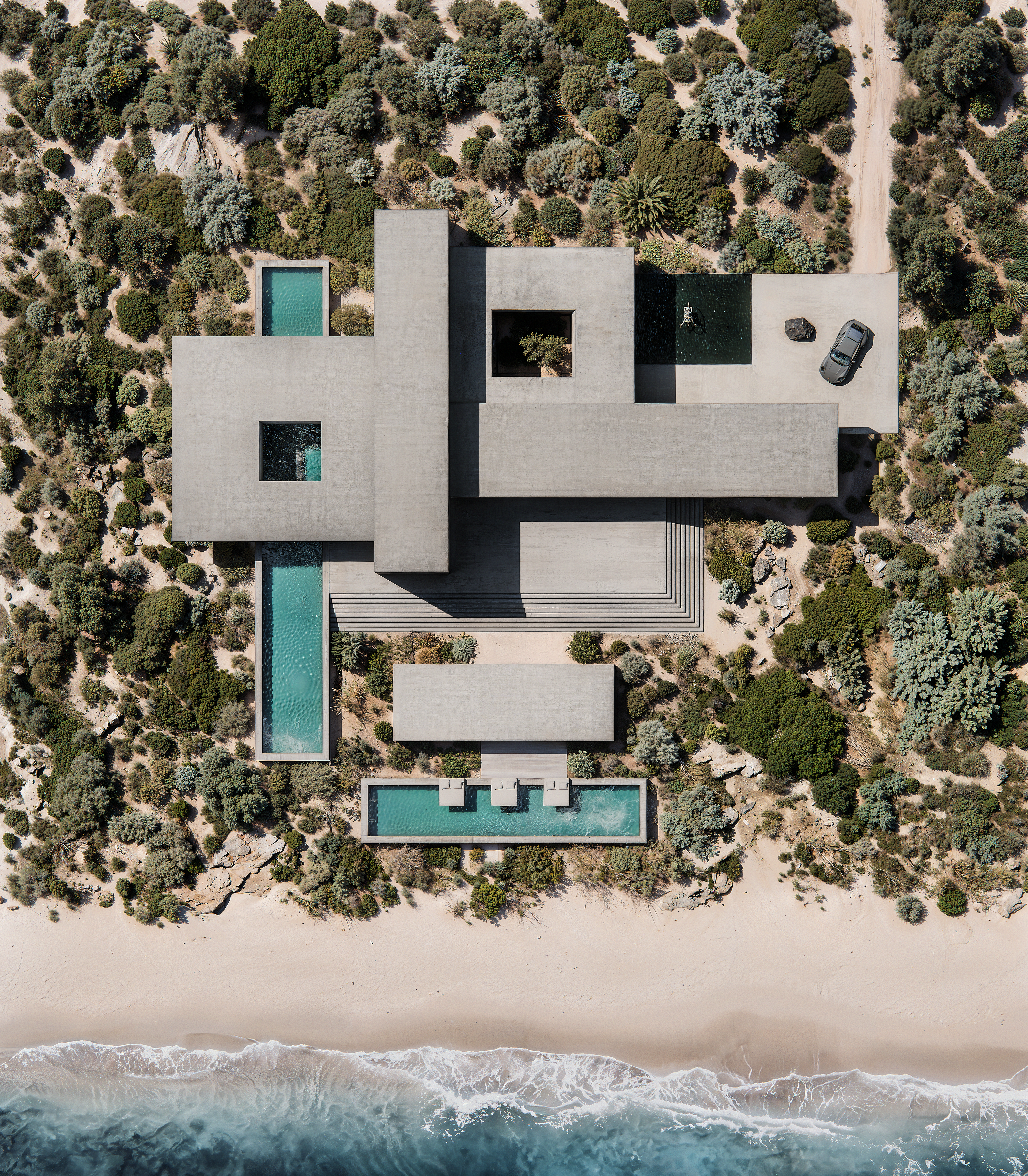 Aerial view of a modernist Caribbean estate with linked pools framed by bushland and beach