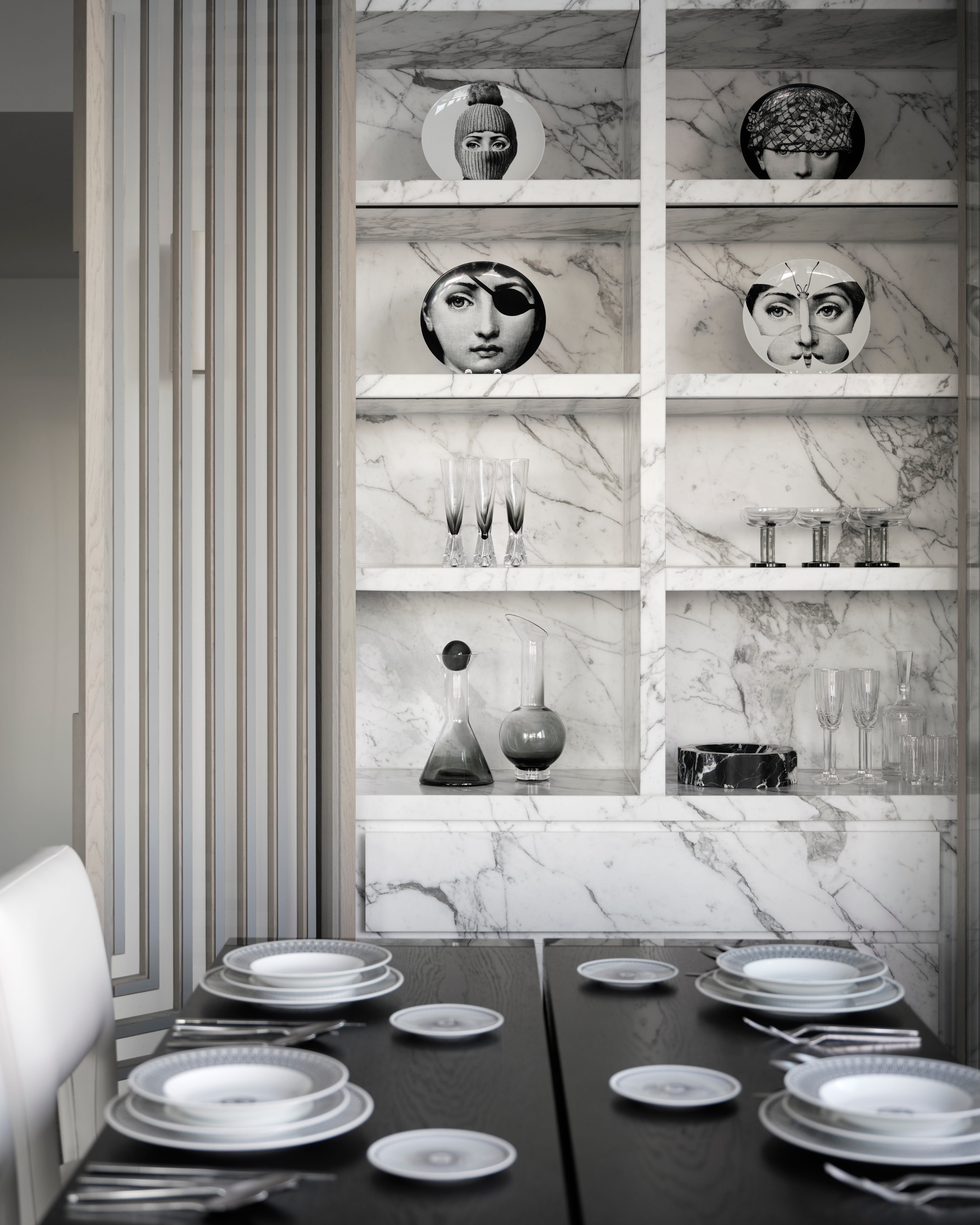 Marble shelving of Fornasetti-style face plates above a dark table laid with white china