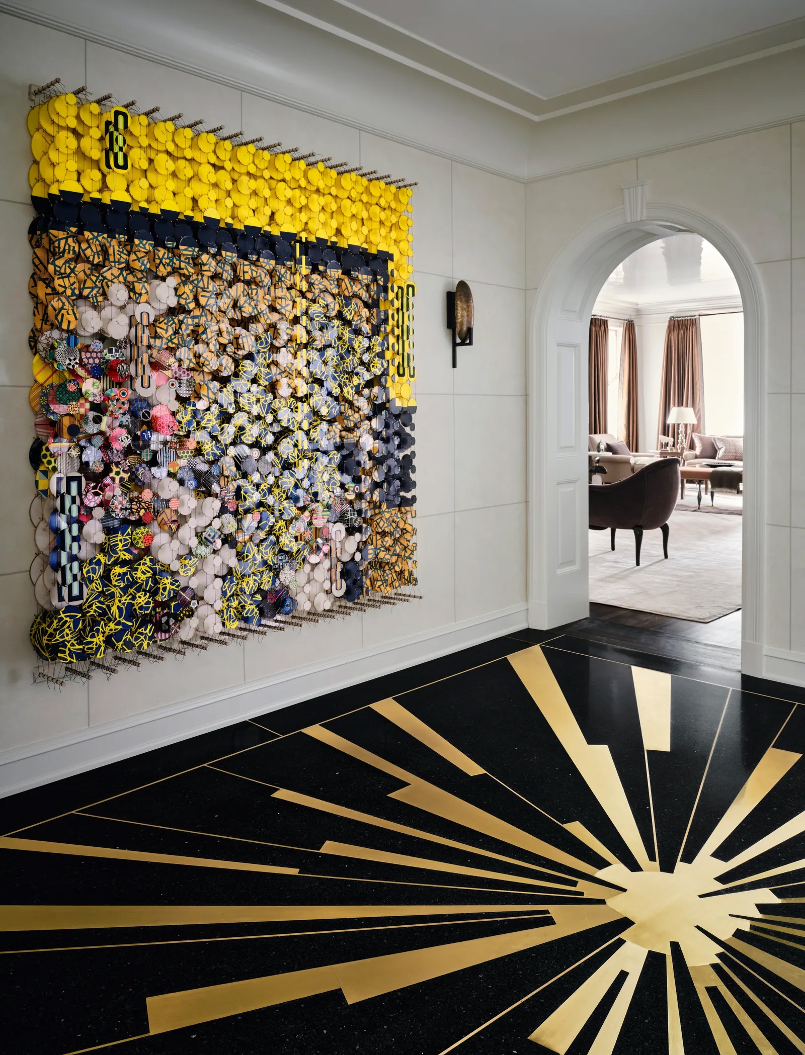 Entrance hall pairing a vivid textile artwork with a black-and-gold sunburst floor