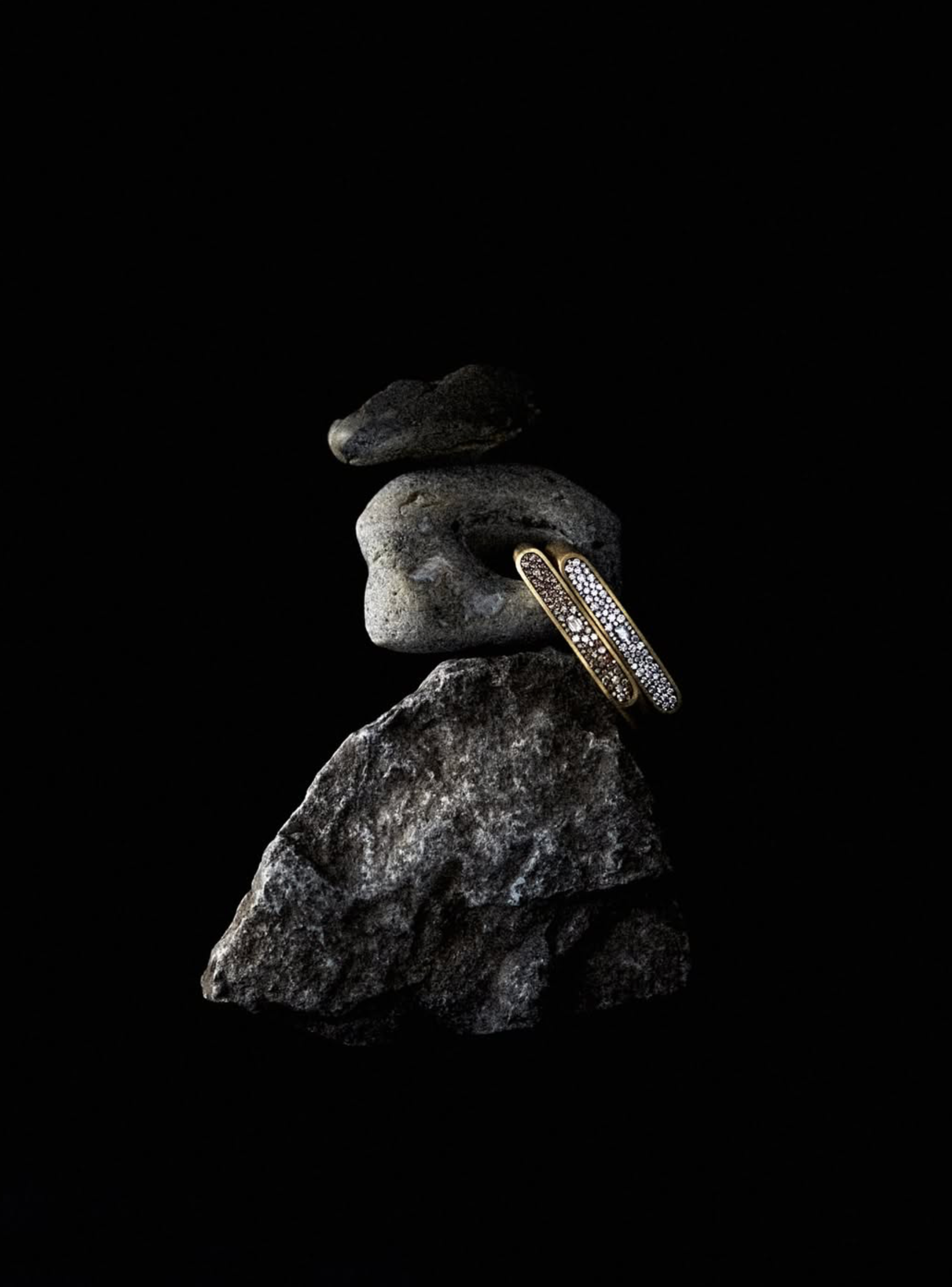 Diamond band resting on a rough grey stone, spotlit against a black background