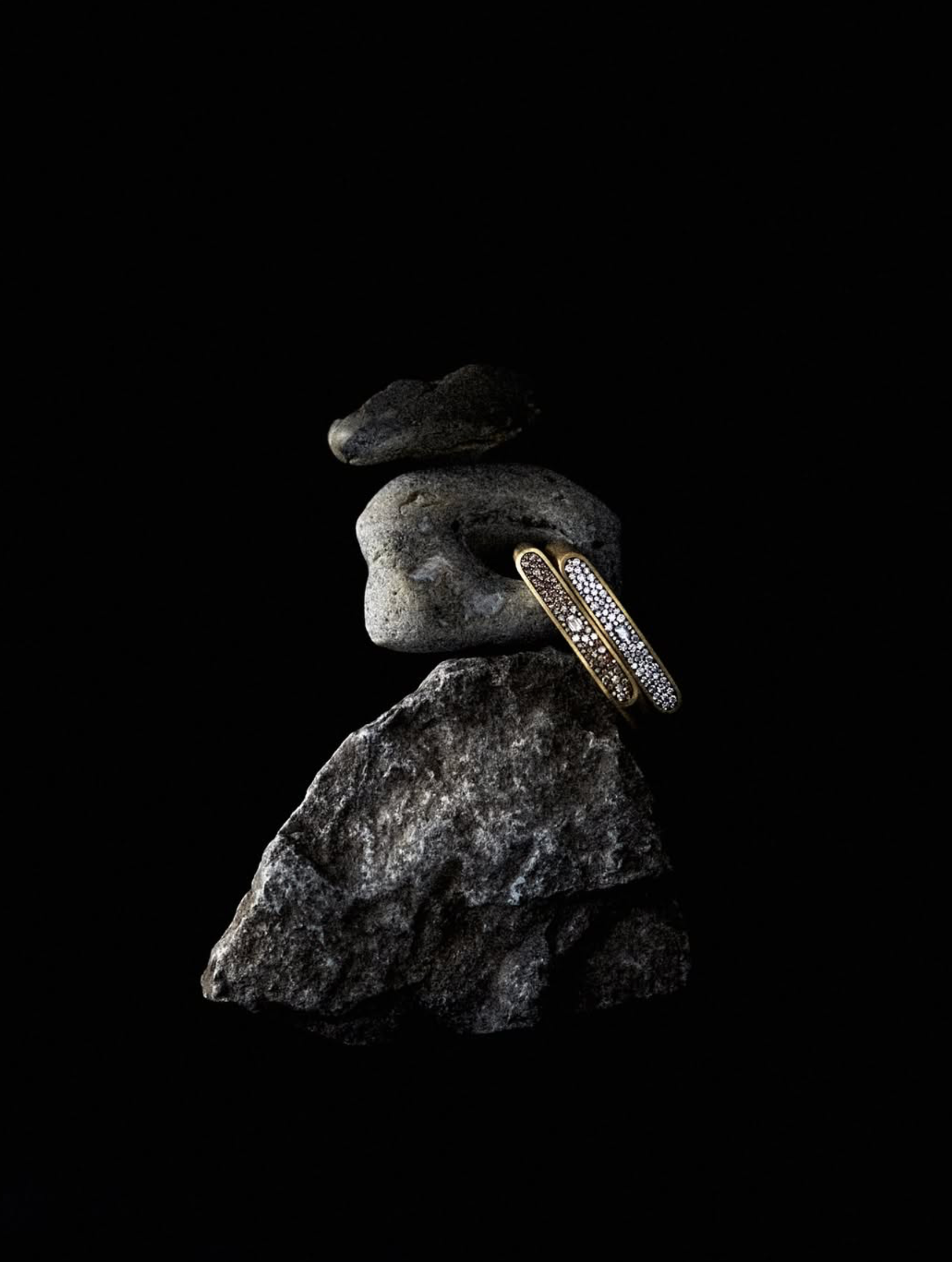 Diamond band resting on a rough grey stone, spotlit against a black background
