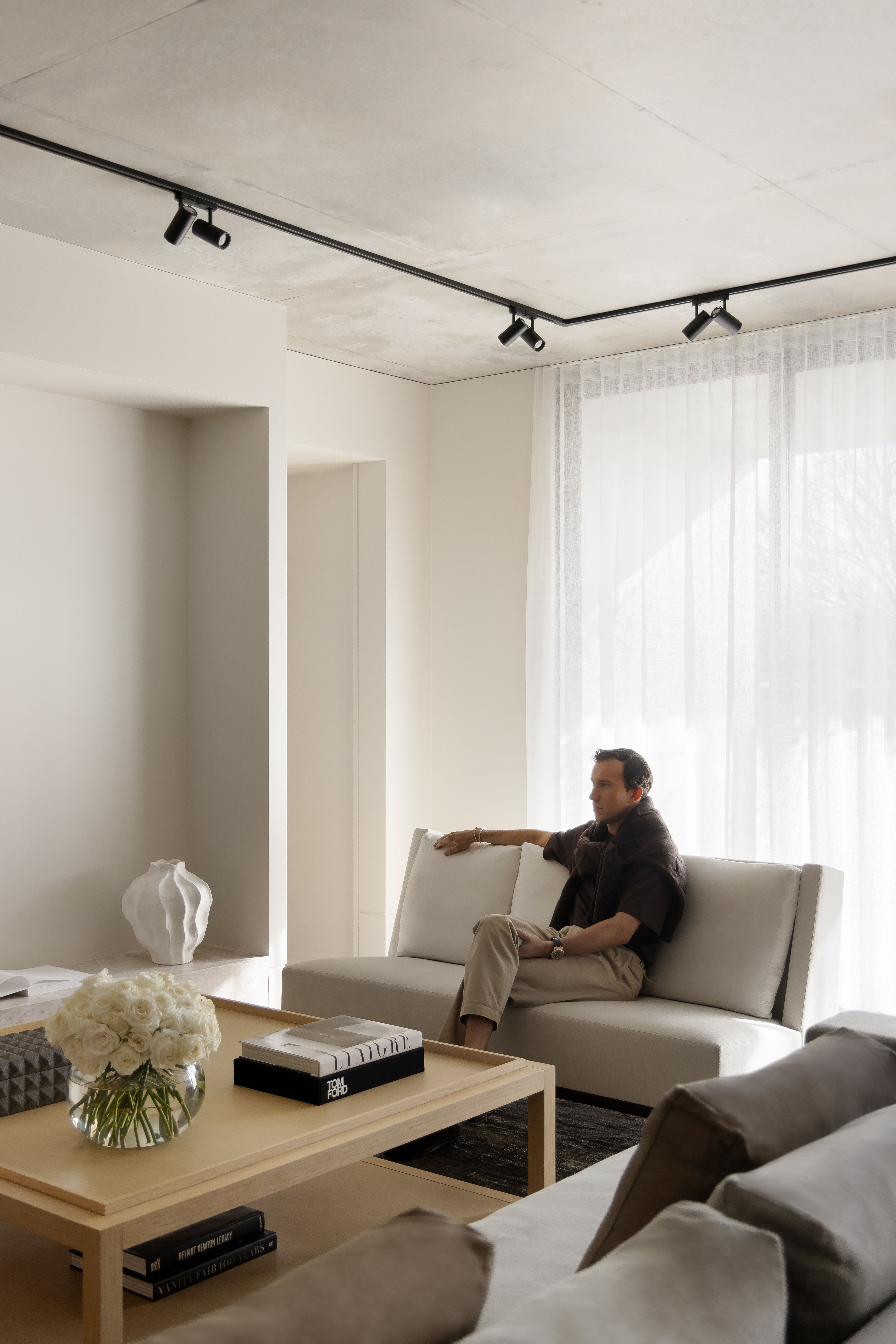Relaxed figure on a taupe sofa beside a low table stacked with books and white blooms