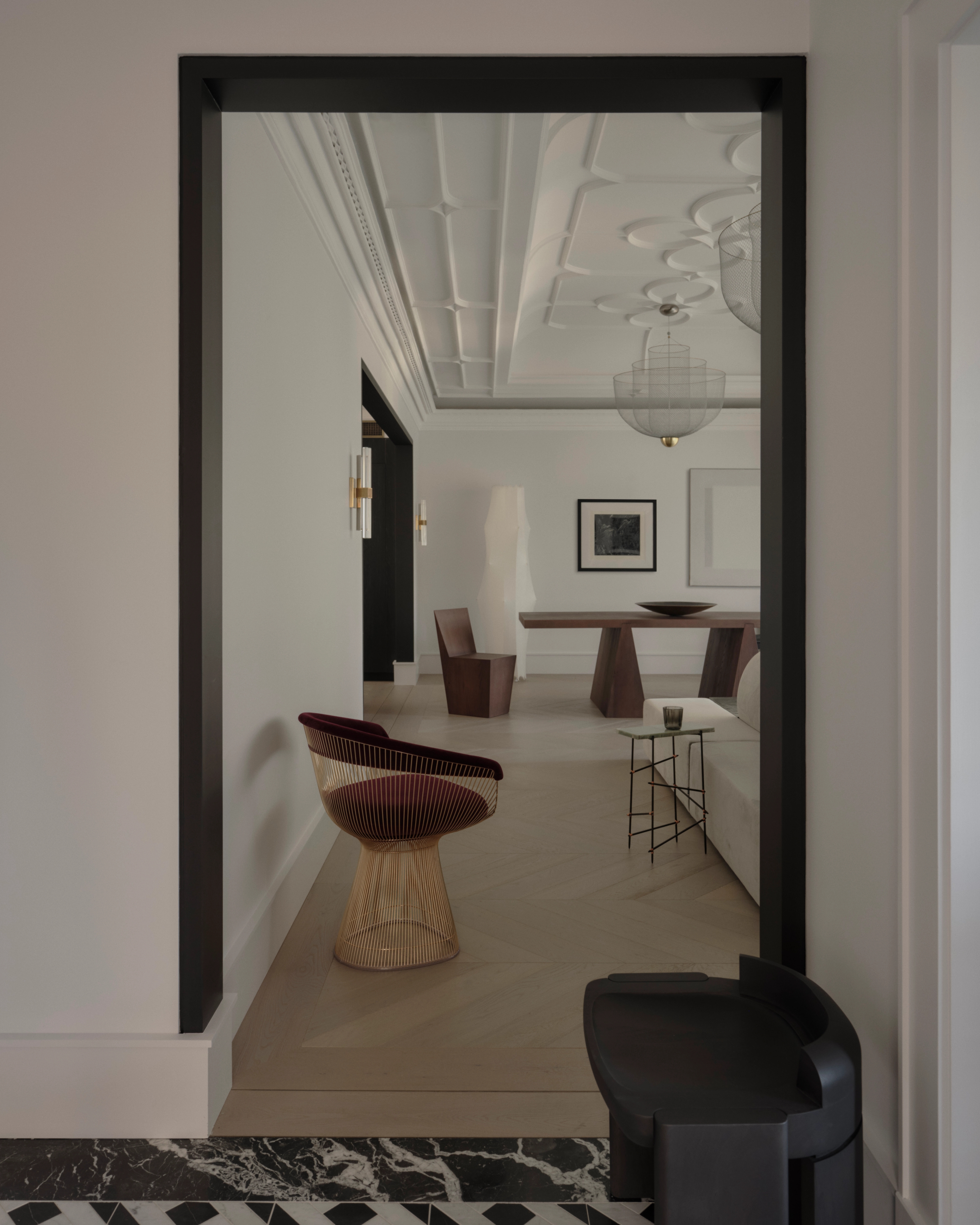 View through a black-framed portal into a Vaucluse room with tan chairs and patterned marble