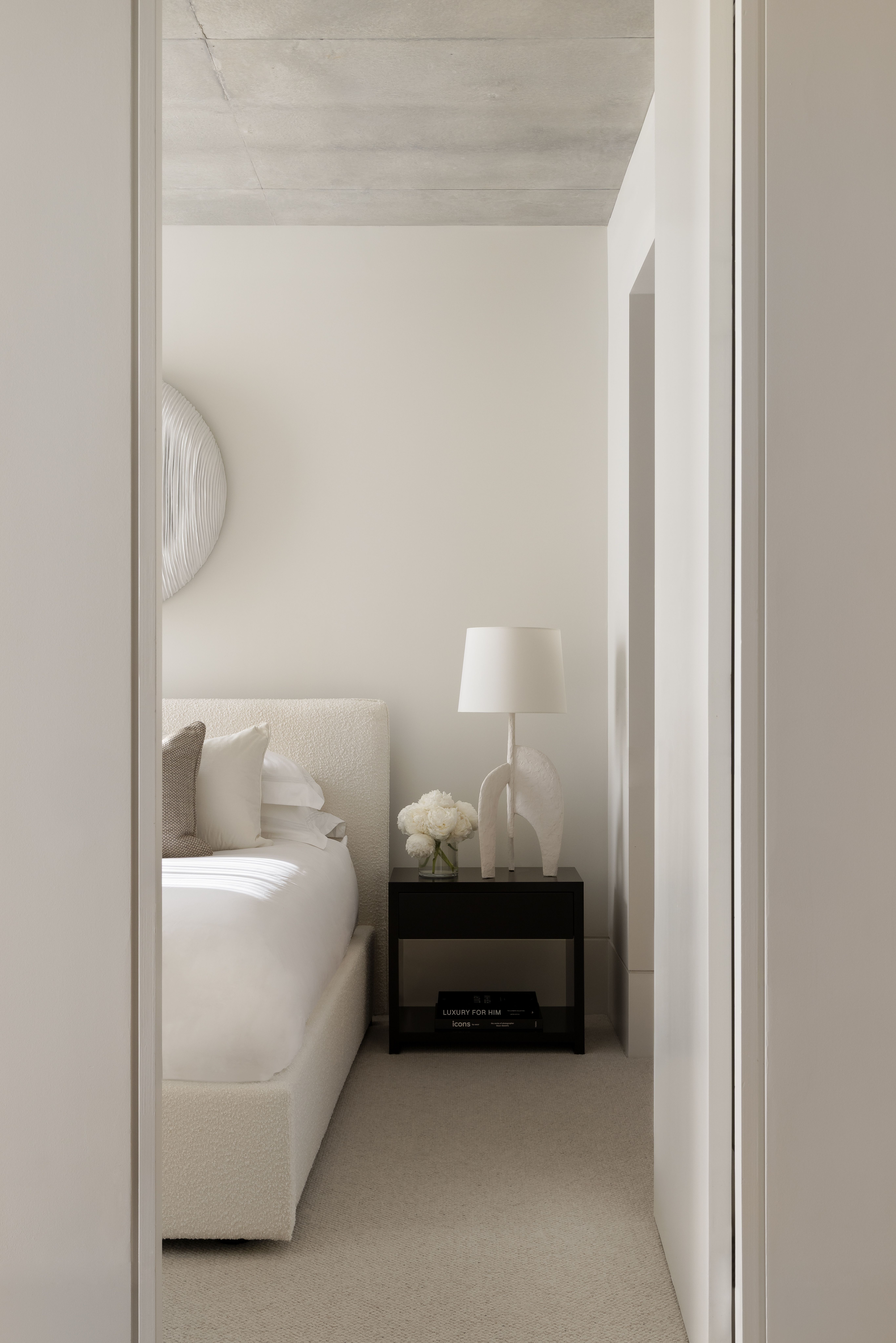 Glimpse through a doorway to a softly neutral bedroom with a bedside lamp