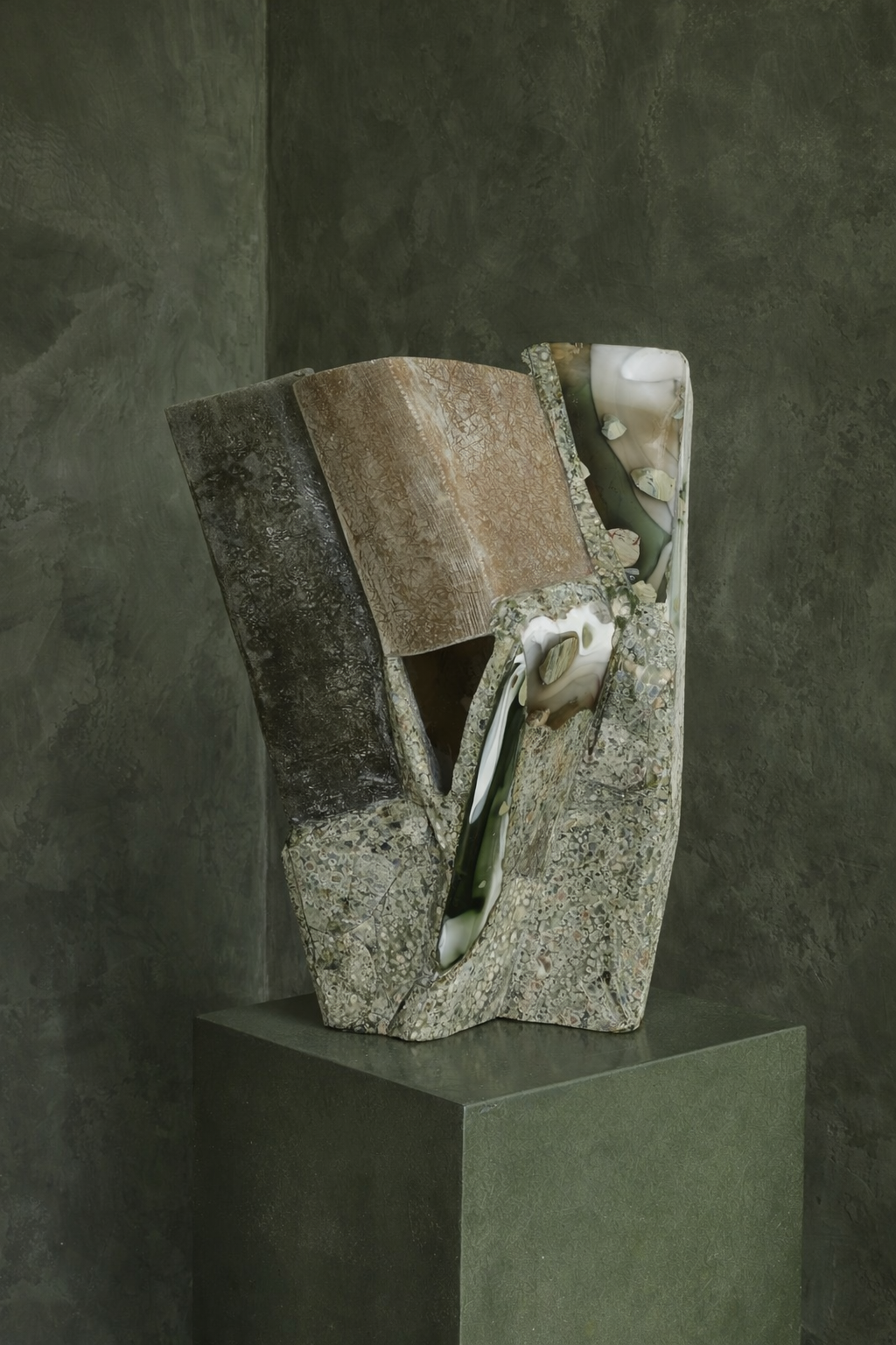 Carved stone artwork on a plinth against a deep green plaster wall in a Vaucluse interior