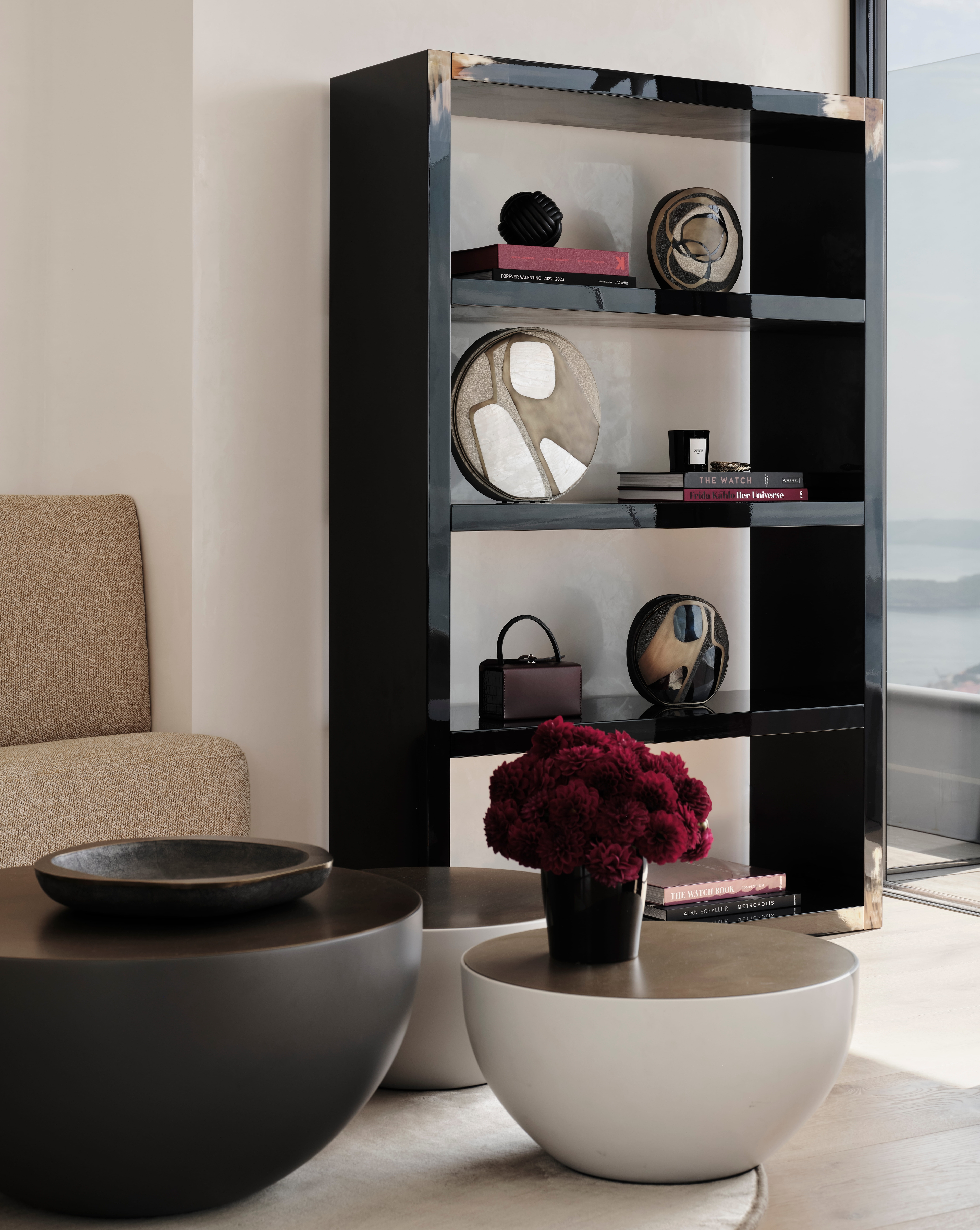 Black modular shelving styled with books and red roses above sculptural bowls in a bright room